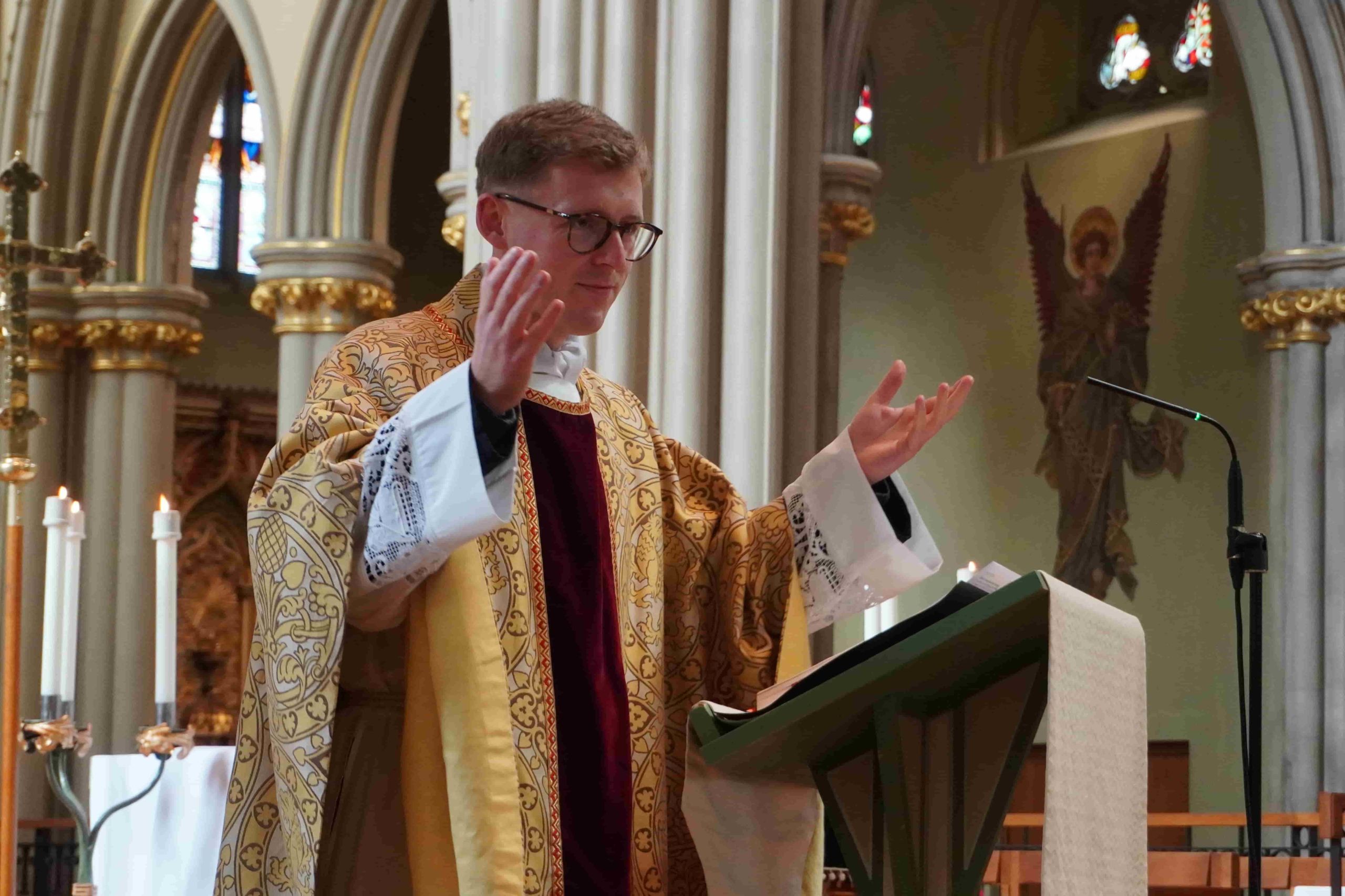 Fr Ryan Browne wearing priestly clothes and with his hands raised open during mass of the feast of the dedication of St John's Cathedral in 2026